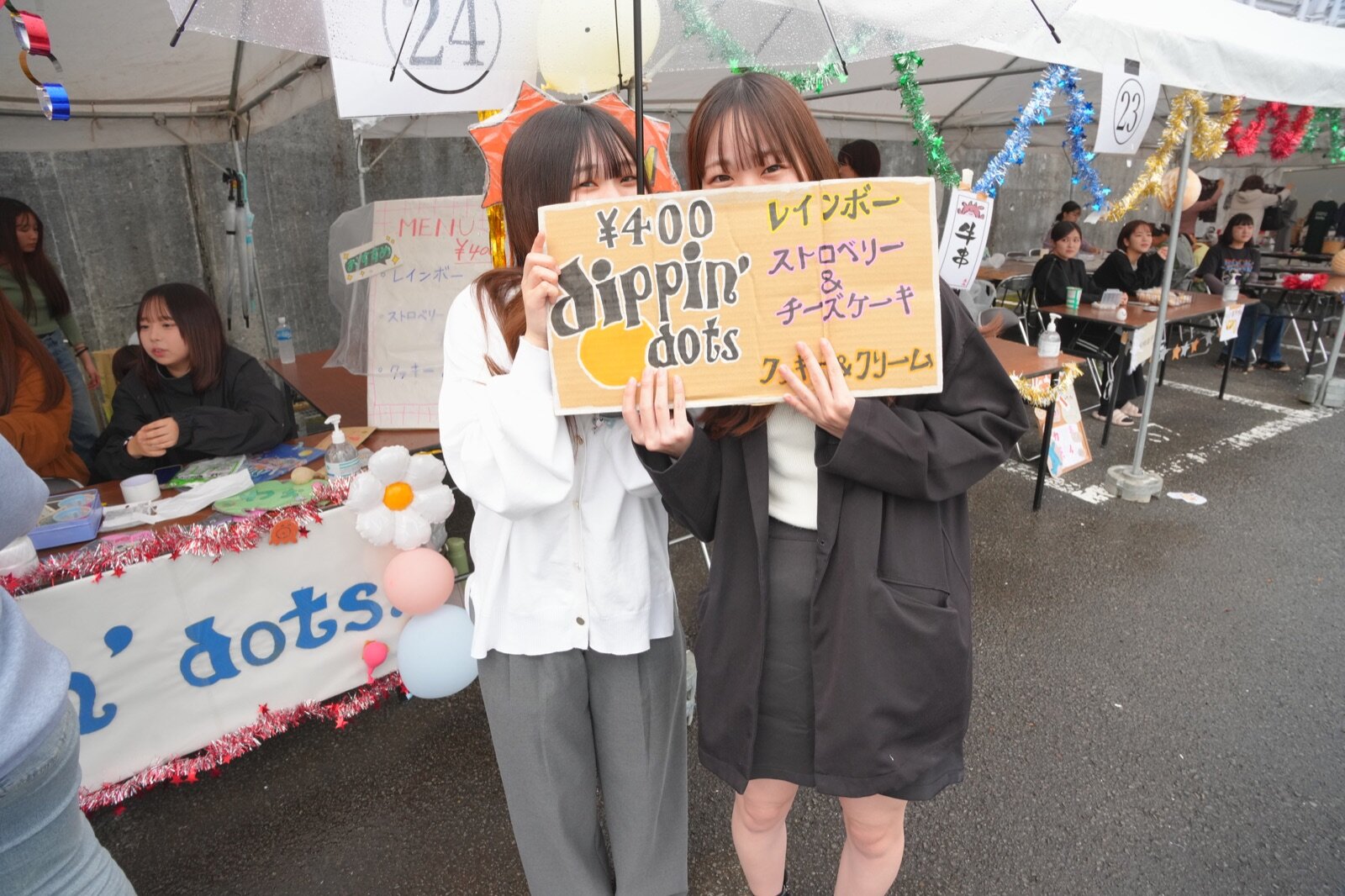 雨の中、模擬店で看板を持つ学生