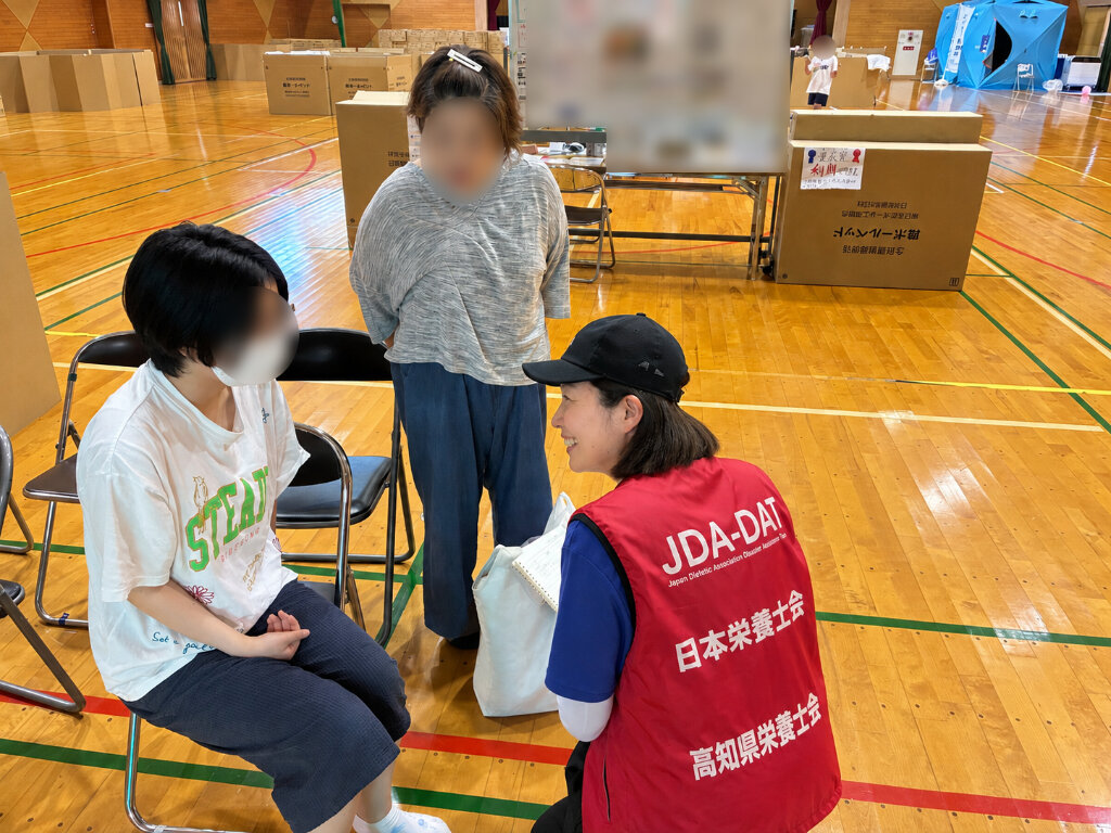 体育館の避難所で、避難者の話を聞く支援スタッフ
