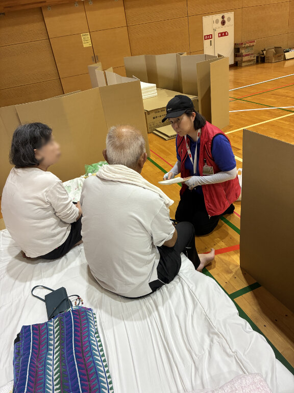 避難所のベッドのそばで避難者の話を聞く様子